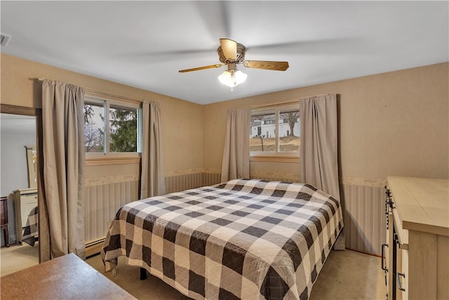 bedroom with visible vents, light colored carpet, a baseboard heating unit, and a ceiling fan