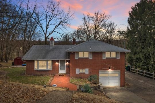 split level home with a garage, brick siding, driveway, and a chimney