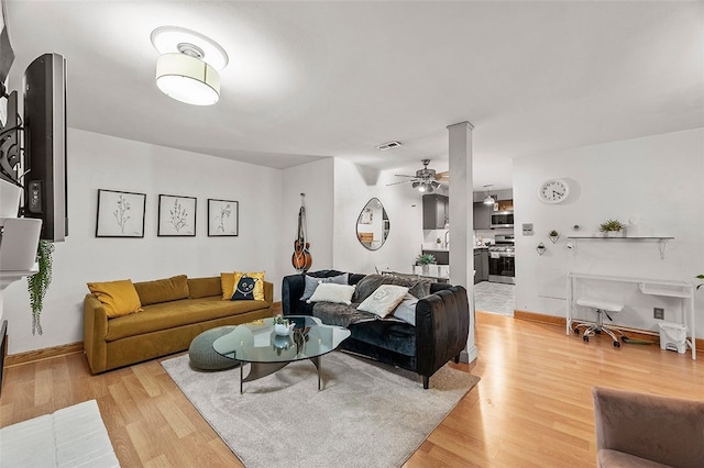 living room featuring visible vents, baseboards, a ceiling fan, and light wood finished floors