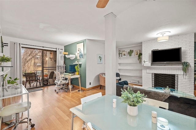 dining space with built in features, a brick fireplace, baseboards, and wood finished floors