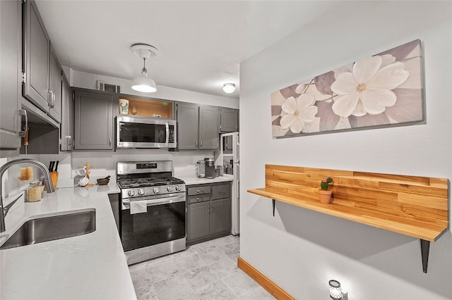 kitchen with gray cabinetry, baseboards, light countertops, appliances with stainless steel finishes, and a sink