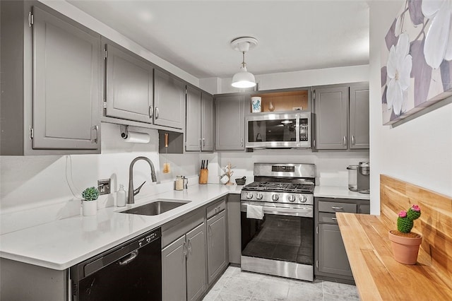 kitchen with open shelves, a sink, gray cabinetry, stainless steel appliances, and wood counters