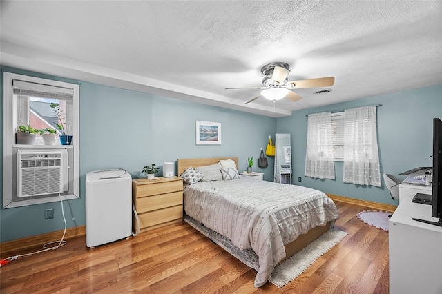 bedroom featuring visible vents, baseboards, wood finished floors, a textured ceiling, and a ceiling fan