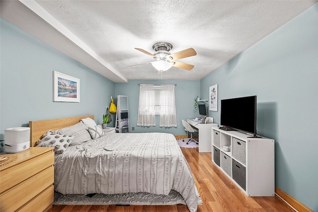 bedroom featuring a ceiling fan, wood finished floors, baseboards, and a textured ceiling