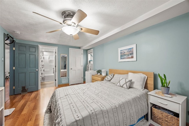 bedroom featuring a textured ceiling, ensuite bathroom, a ceiling fan, and wood finished floors