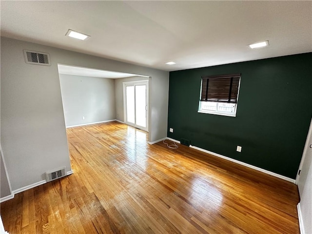 empty room with light wood finished floors, visible vents, and baseboards