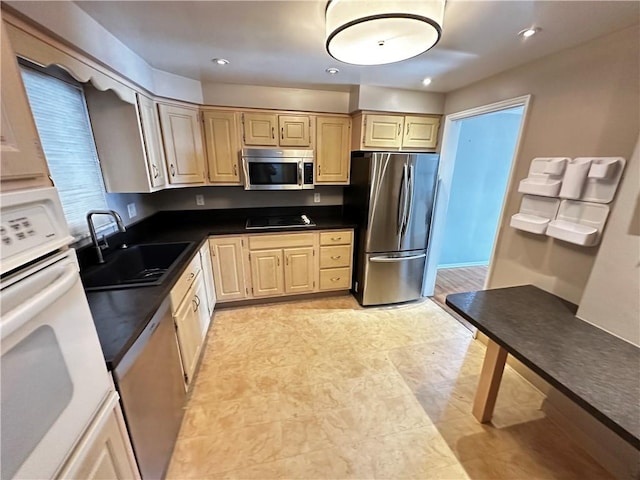 kitchen with recessed lighting, a sink, light brown cabinetry, stainless steel appliances, and dark countertops