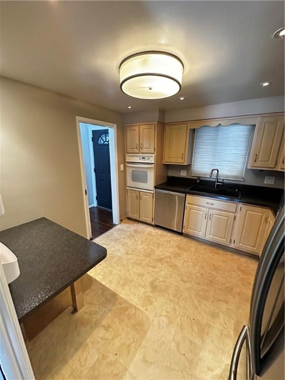 kitchen with dark countertops, light brown cabinets, a sink, dishwasher, and white oven