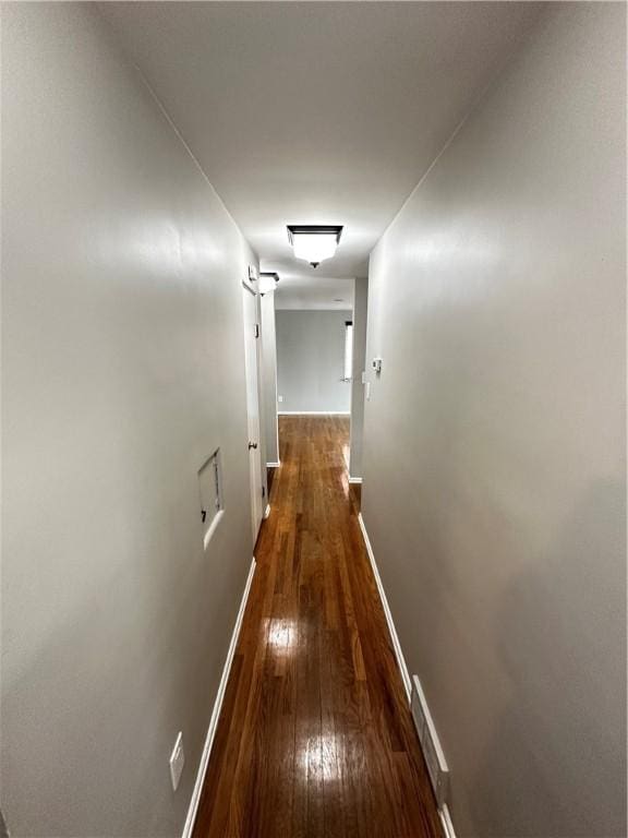 hallway with visible vents, baseboards, and hardwood / wood-style flooring