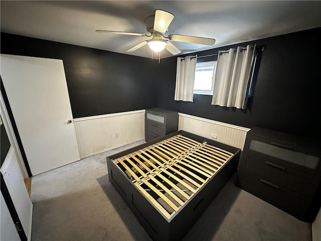 carpeted bedroom featuring a wainscoted wall and a ceiling fan