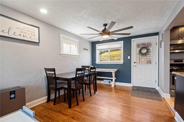 dining room with baseboards, visible vents, ceiling fan, a textured ceiling, and light wood-type flooring