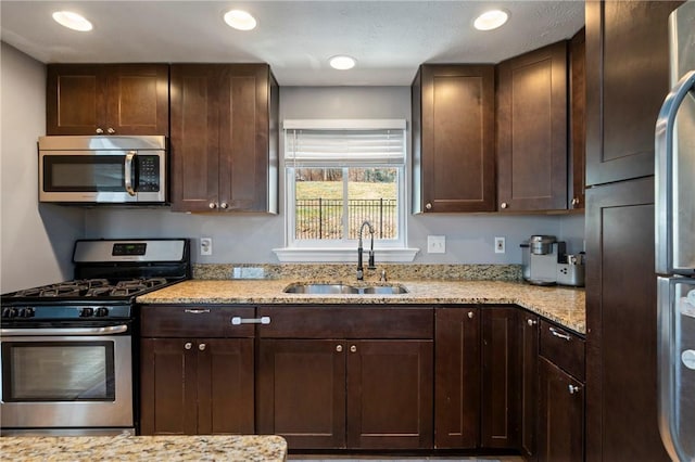 kitchen featuring dark brown cabinetry, light stone countertops, appliances with stainless steel finishes, and a sink