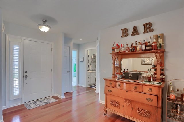 foyer entrance with light wood-style flooring, a bar, and baseboards