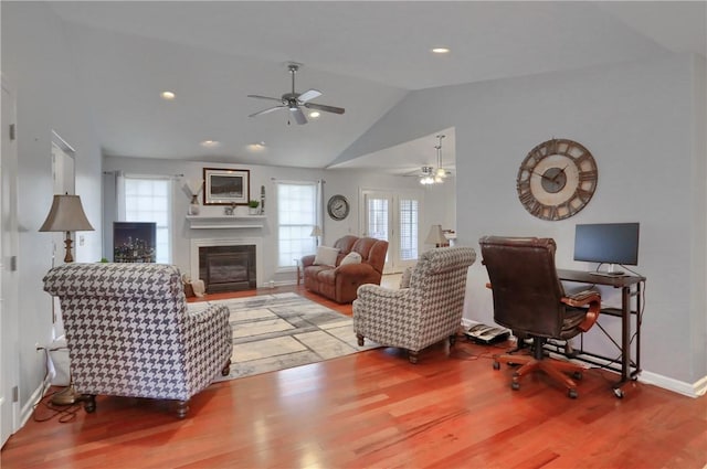 living area featuring lofted ceiling, a ceiling fan, a glass covered fireplace, wood finished floors, and baseboards