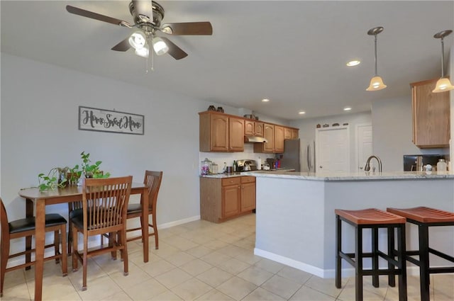 kitchen featuring a peninsula, freestanding refrigerator, a sink, ceiling fan, and under cabinet range hood