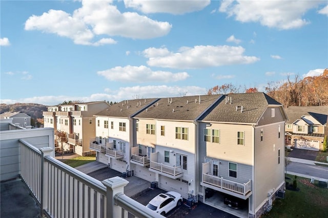 back of house with aphalt driveway, a balcony, an attached garage, and a residential view