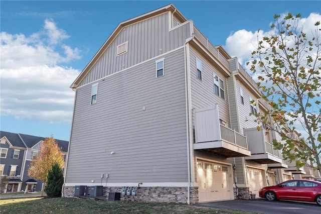 view of property exterior featuring central air condition unit, board and batten siding, driveway, and a garage