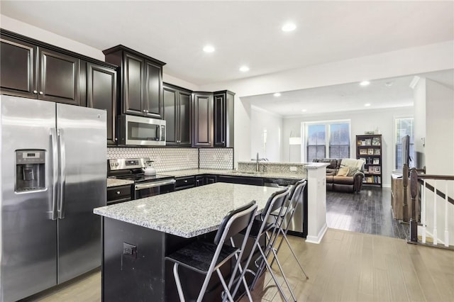 kitchen featuring light stone countertops, appliances with stainless steel finishes, light wood-style flooring, and open floor plan