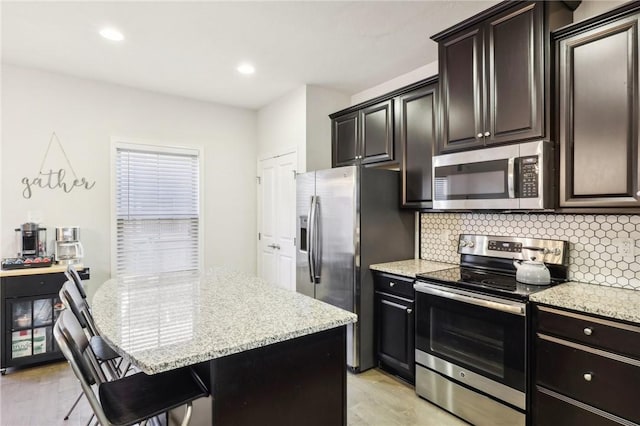 kitchen featuring light stone counters, decorative backsplash, appliances with stainless steel finishes, and a breakfast bar