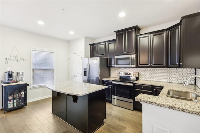 kitchen with light wood-style flooring, a sink, decorative backsplash, stainless steel appliances, and a center island