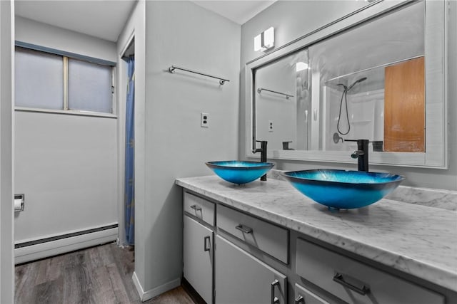 full bath with double vanity, wood finished floors, baseboard heating, and a sink