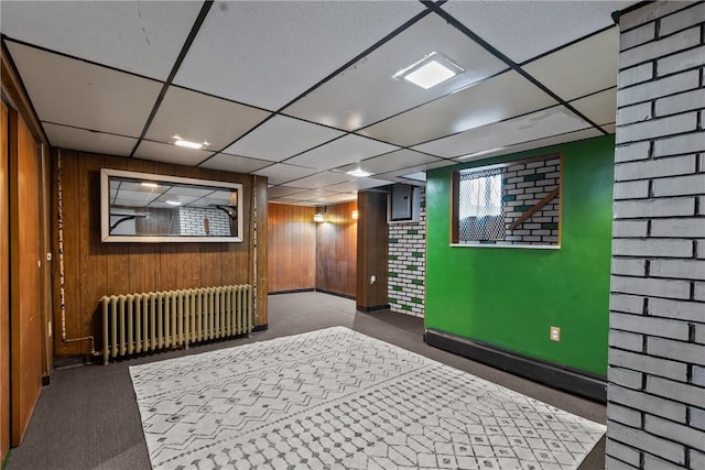 interior space with a drop ceiling, radiator heating unit, and wood walls