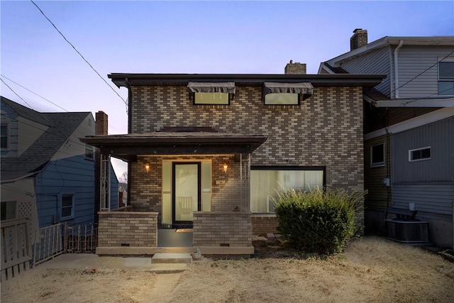 view of front of property featuring brick siding, a porch, a chimney, and central AC