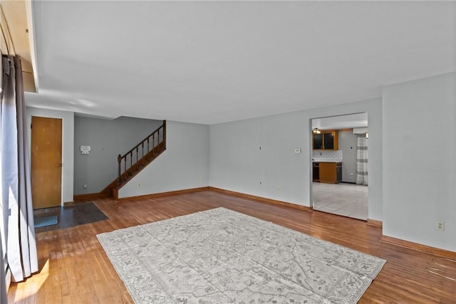 unfurnished living room with stairs, baseboards, and light wood finished floors