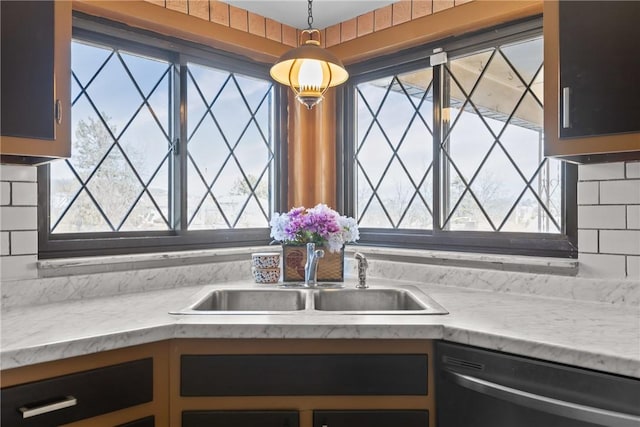 kitchen featuring a sink, hanging light fixtures, light countertops, stainless steel dishwasher, and tasteful backsplash