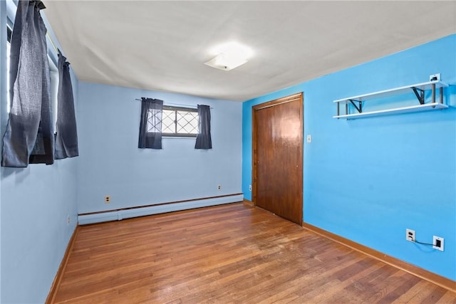 unfurnished bedroom featuring a baseboard heating unit, baseboards, and wood finished floors