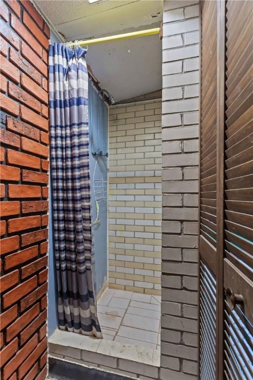 bathroom featuring curtained shower and brick wall