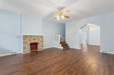 unfurnished living room featuring wood finished floors, visible vents, arched walkways, ceiling fan, and stairs