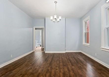 spare room featuring dark wood finished floors, an inviting chandelier, and baseboards