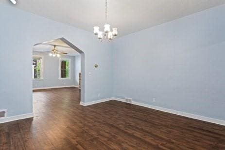 unfurnished room with arched walkways, ceiling fan with notable chandelier, dark wood-type flooring, and baseboards