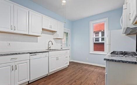 kitchen with white appliances, white cabinets, stone countertops, and a sink