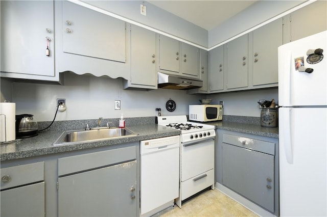 kitchen with white appliances, gray cabinetry, a sink, under cabinet range hood, and dark countertops