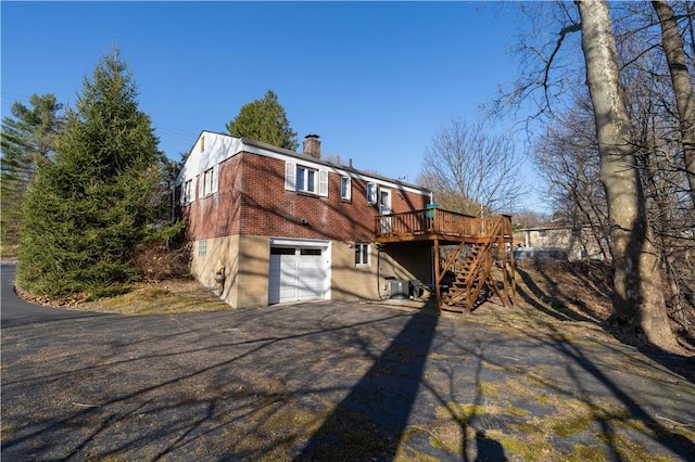 exterior space featuring driveway, a chimney, stairs, a garage, and brick siding