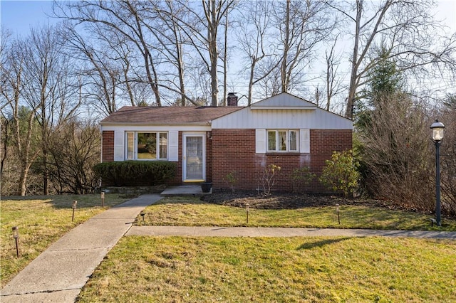 view of front of property featuring brick siding, a chimney, and a front lawn