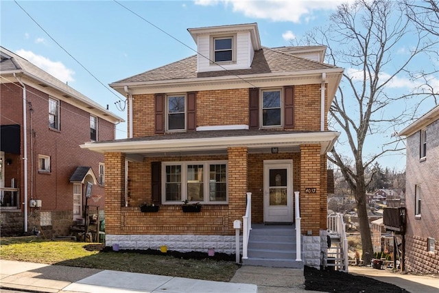 american foursquare style home with brick siding, a porch, entry steps, and roof with shingles