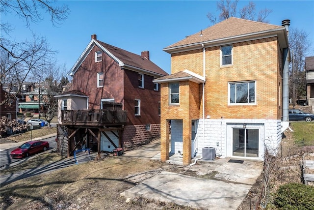 rear view of property with brick siding, a shingled roof, central AC unit, a deck, and a patio