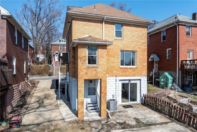 back of property with a patio, brick siding, roof with shingles, and central AC