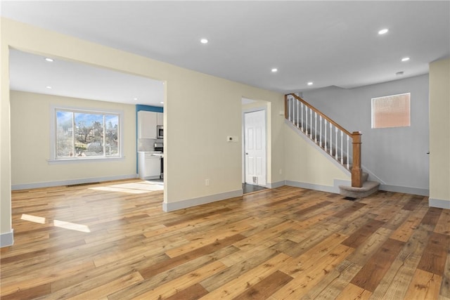 unfurnished living room featuring recessed lighting, light wood-type flooring, and stairs