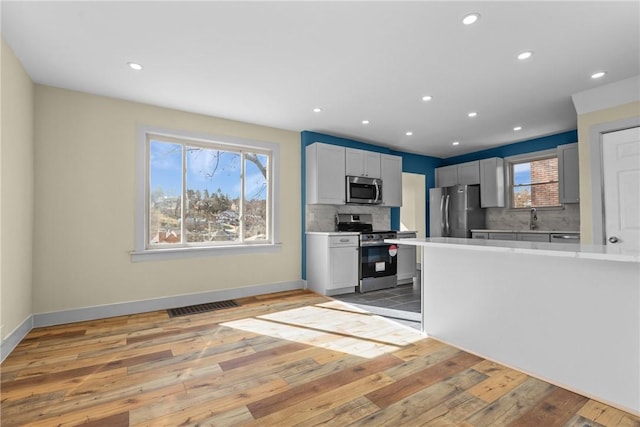 kitchen with visible vents, light wood-style flooring, stainless steel appliances, light countertops, and backsplash