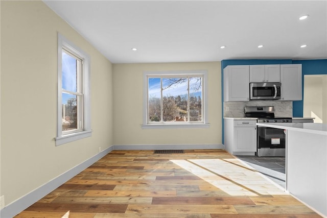 kitchen featuring stainless steel appliances, baseboards, tasteful backsplash, and light wood-style flooring