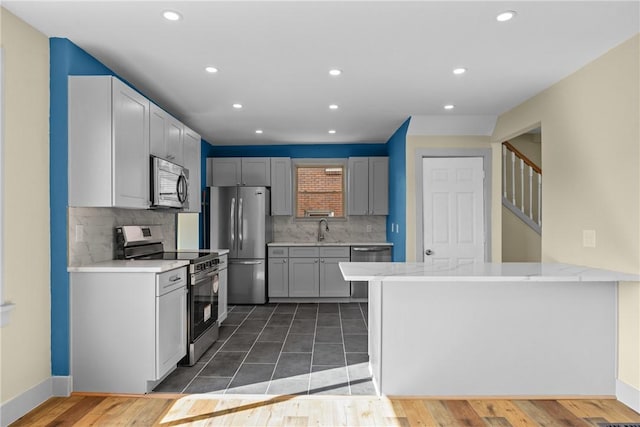 kitchen with recessed lighting, appliances with stainless steel finishes, a peninsula, wood finished floors, and a sink