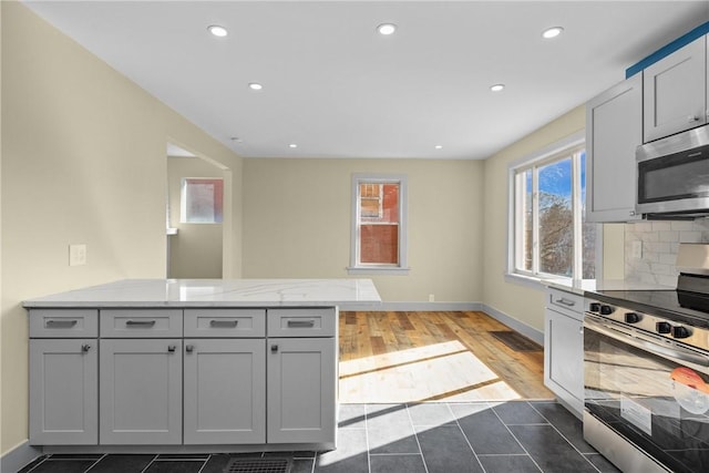 kitchen with a peninsula, dark tile patterned flooring, gray cabinets, stainless steel appliances, and tasteful backsplash