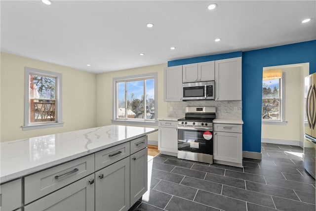 kitchen featuring light stone countertops, baseboards, recessed lighting, stainless steel appliances, and backsplash