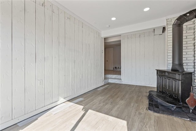 living room featuring wood finished floors, baseboards, a wood stove, recessed lighting, and ornamental molding