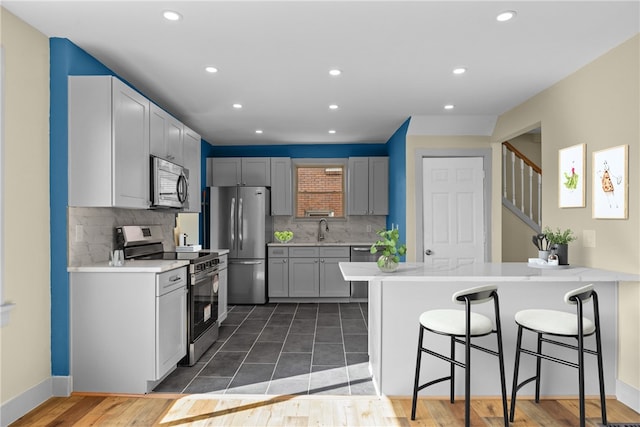 kitchen featuring a breakfast bar, a peninsula, a sink, stainless steel appliances, and light countertops