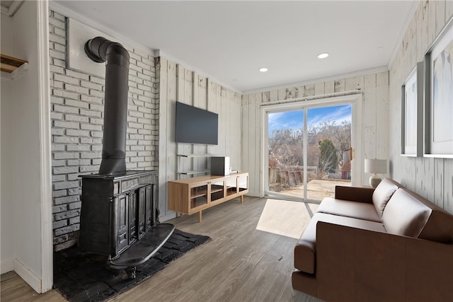 living area with baseboards, wood finished floors, a wood stove, and crown molding